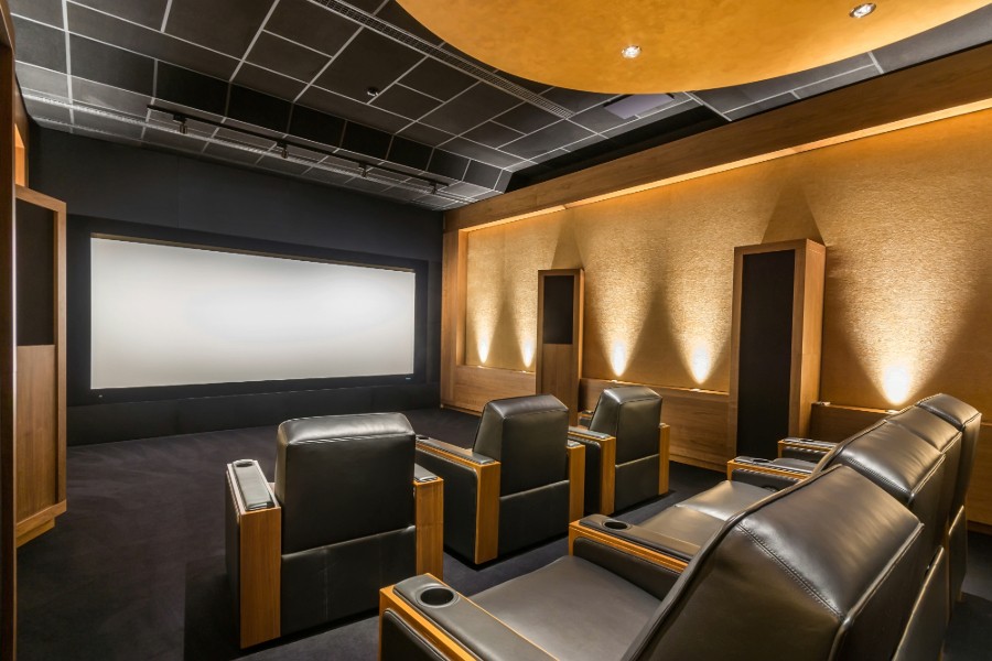 A home theater room featuring a large projector screen, surrounded by several black reclining chairs. 