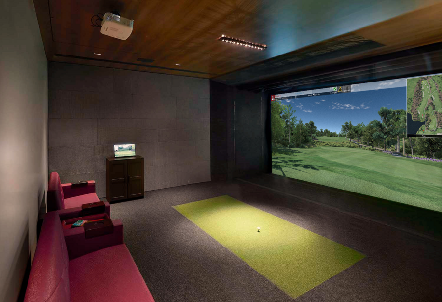 A golf simulator/media room with projector, large screen, sofa seating, and golf green area.