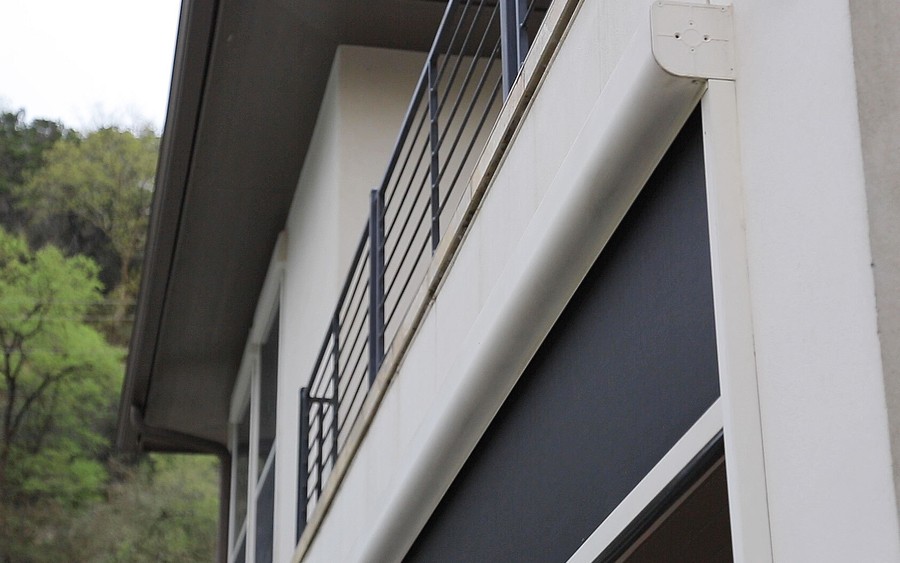 A Screen Innovations outdoor screen partially lowered below a home’s balcony.
