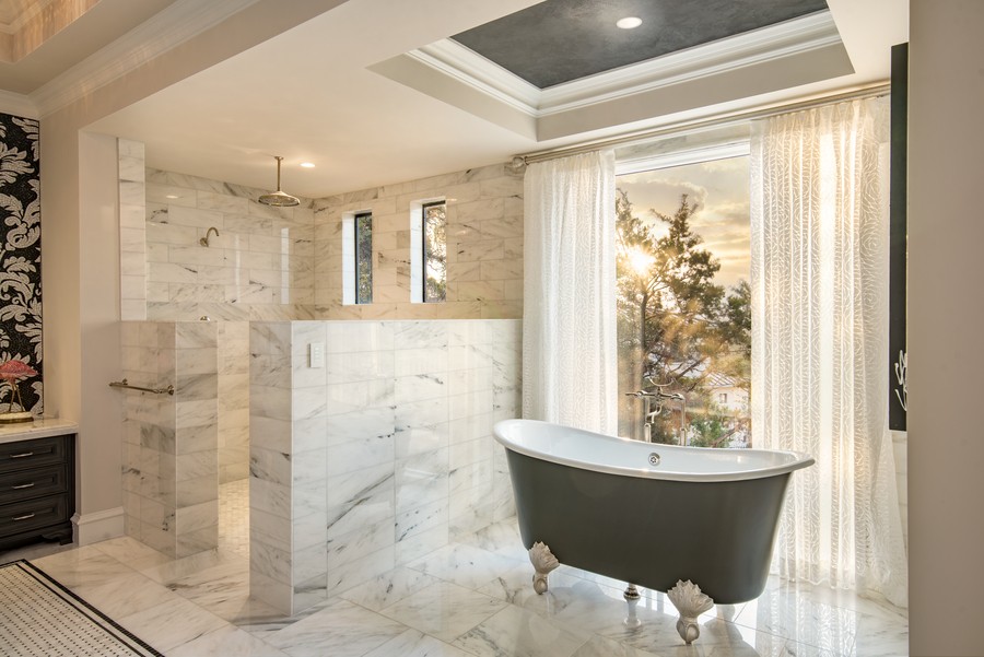 A bathroom with a clawfoot tub illuminated by soft, warm lighting and sunlight peering in the window.