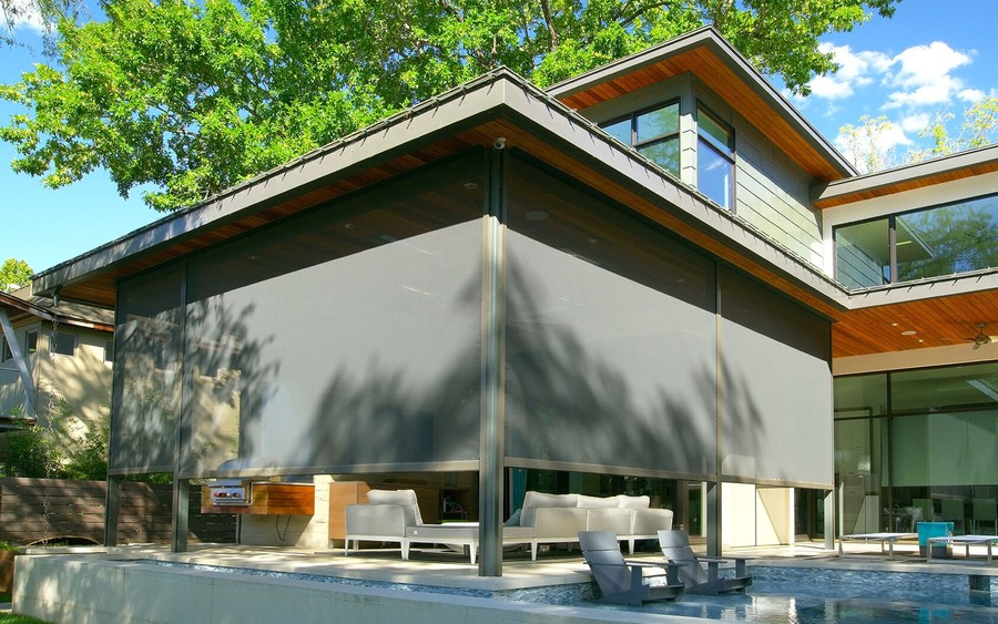 A house with outdoor shades lowered on the patio next to an in-ground pool. 